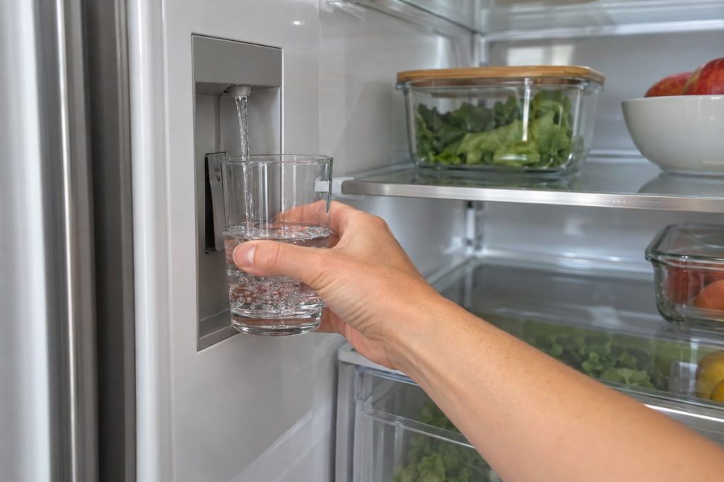 Hand holds a glass under a thin stream from the internal water dispenser